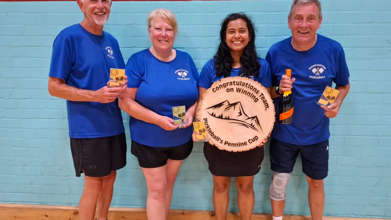 Four pickleball club players in matching blue printed club t-shirts holding a trophy